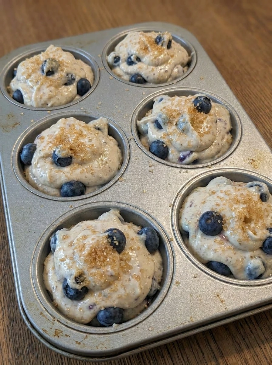 Blueberry muffin batter portioned into muffin tin with sugar on top