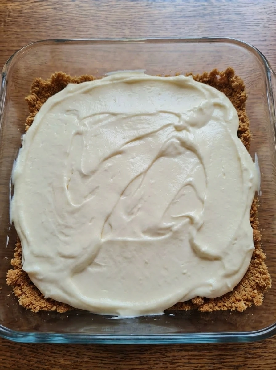 Cream cheese filling spread over pressed graham cracker crust in baking dish