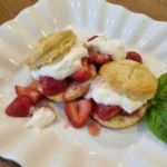 Classic Strawberry Shortcake on a white scalloped dessert plate with juicy strawberries and whipped cream