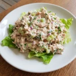 Creamy Tuna Salad served on a white plate with lettuce leaves and visible celery and red onion.