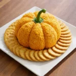 Halloween Appetizers Cheese Ball shaped like a pumpkin with shredded cheddar, a green pepper stem and round crackers