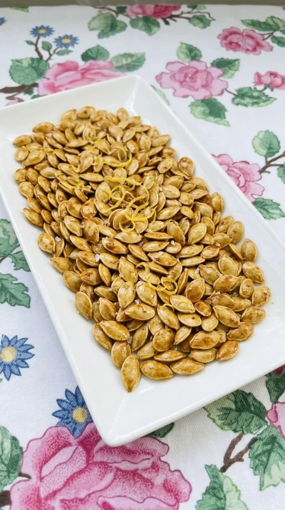 Lemon Roasted Pumpkin Seeds piled on a white platter with golden edges, paprika speckles and fresh lemon Recipe focus: how to make lemon roasted pumpkin seeds.