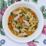 Gluten Free Chicken Noodle Soup with shredded chicken, carrots, celery and wide noodles in golden broth