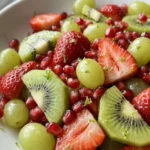 Christmas Fruit Salad with red strawberries, green kiwi, grapes and pomegranate seeds in a white serving bowl Recipe focus: christmas salad.