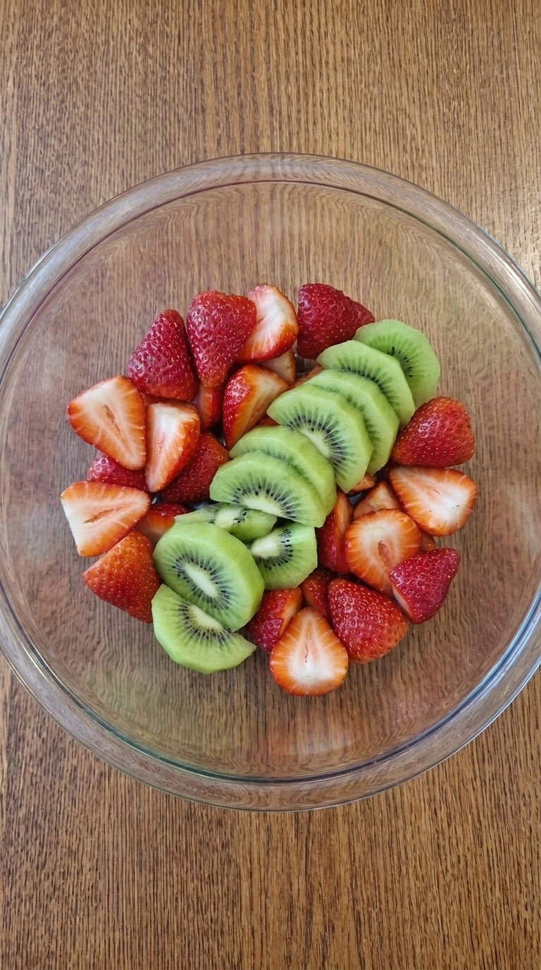Christmas Fruit Salad preparation with halved strawberries and thin green kiwi slices in a mixing bowl Recipe focus: green christmas salad.