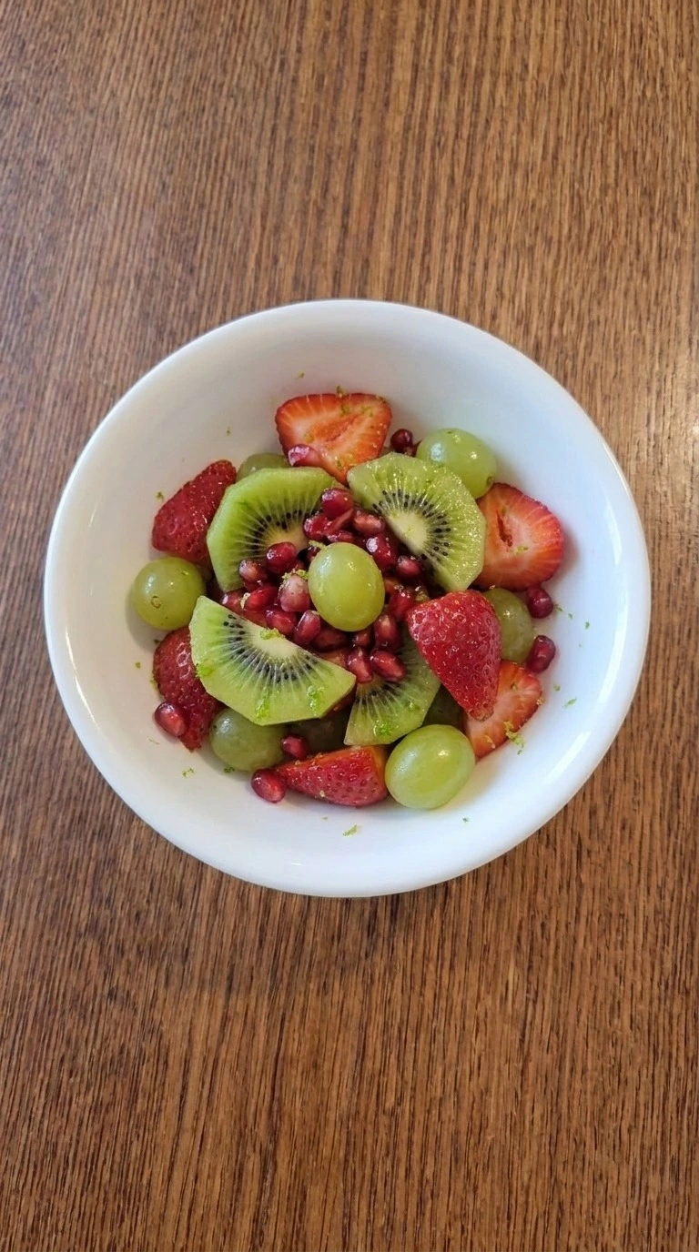 Christmas Fruit Salad served in a small white bowl with fresh strawberries, kiwi, grapes and pomegranate Recipe focus: green christmas salad.