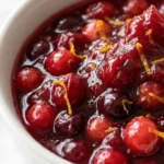 Cranberry Orange Sauce in a white serving bowl with glossy ruby-red berries and fresh orange zest. Recipe focus: easy cranberry orange sauce.