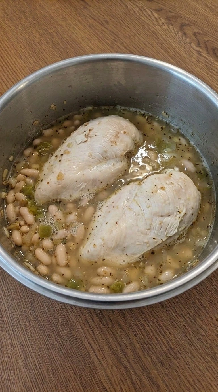 Creamy White Chicken Chili with two chicken breasts simmering among white beans and diced green chiles. Recipe focus: crockpot white chicken chili.