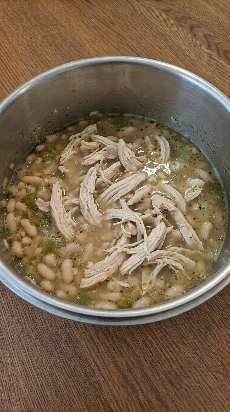 Creamy White Chicken Chili thickening with shredded chicken and partially mashed cannellini beans. Recipe focus: crockpot white chicken chili.